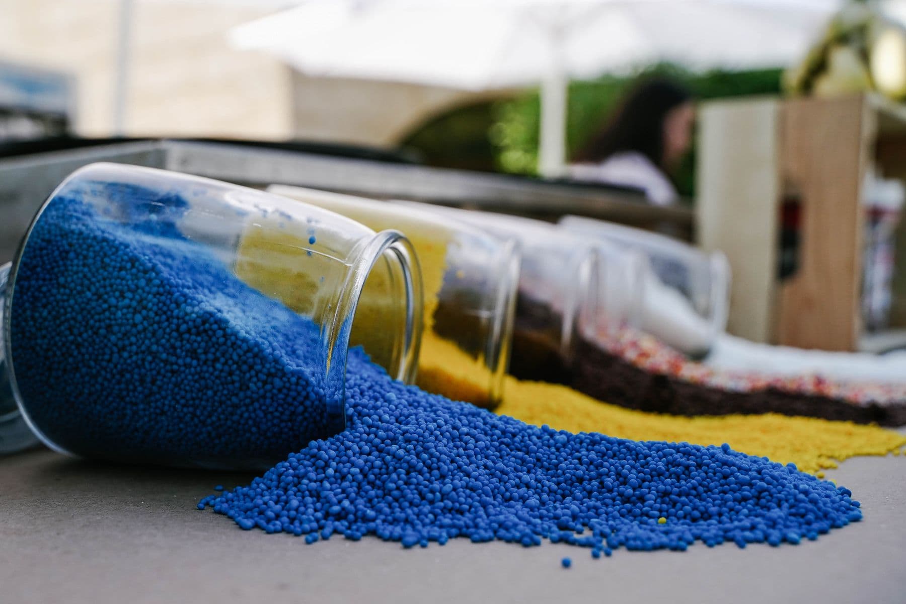 Macro of vibrant blue, yellow and white masterbatch pellets spilling from a jar